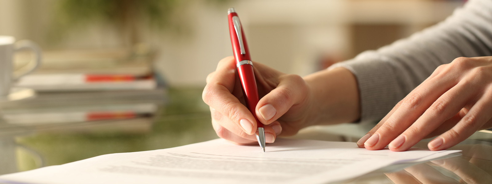 woman signing document with pen on a desk at home